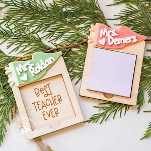 Op de afbeelding: Twee houten lerarencadeaus met gepersonaliseerde naambanners. Eén banner is groen met "Mrs. Roldan" en de andere is roze met "Mrs. Demers". Het eerste frame zegt "Best Teacher Ever". Elk frame heeft ruimte voor een notitie.