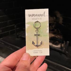 May include: A silver anchor keychain with the word "immanuel" and the text "God with us" on a white card with a green watercolor background. The card also includes the text "Isaiah 7:14".