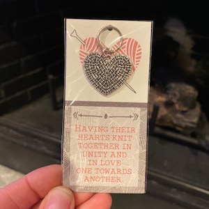 May include: A silver heart-shaped knitting stitch marker with a key ring. The marker is packaged on a card with the text "Having their hearts knit together in unity and in love one towards another."