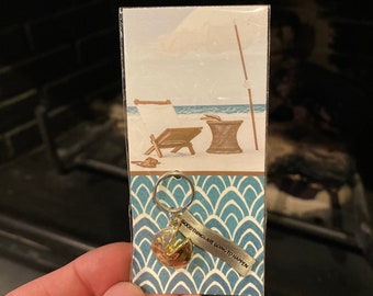 May include: A gold fortune cookie keychain with the text "Good things are going to happen" on a blue and white patterned card.