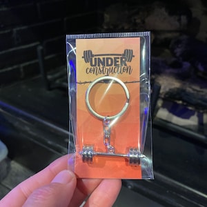 May include: A silver keychain with a barbell design and the words "UNDER construction" on a bright orange card.