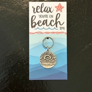May include: A silver keychain featuring a sun and waves design. The keychain is attached to a card with the text "relax you're on beach time" and a red starfish.