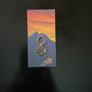 May include: A gold-coloured keychain with a cross charm that says "Bless The Lord Oh My Soul". The keychain is on a card with a sunset and mountain scene.