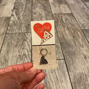 May include: A red heart with the words "You're Slicin' my Heart!" and the word "Pizza" on it. A silver pizza slice charm is attached to a key ring.