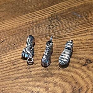 May include: Three silver charms shaped like boots. The charms are detailed and have a worn look.