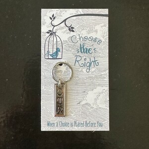 May include: A silver keychain with the word "CHOOSE THE RIGHT" on a white card with a bird in a cage illustration. The text "When a Choice is Placed Before You" is also on the card.