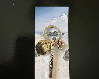 May include: A gold-toned keychain with a heart charm that says "Beautiful" and a charm that says "I am worthy". The keychain also has a small charm with rhinestones.