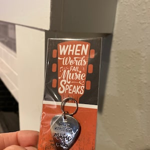 May include: A silver guitar pick keychain with the text "When words fail, music speaks" on a red and black background.