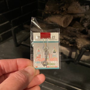 May include: A silver charm with a heart and arrow design. The charm is attached to a silver chain and has the words "Called to Serve Him" and "Only King Chosen Ere for His Name" on it.
