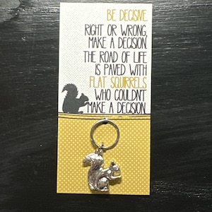 May include: A silver squirrel keyring with a motivational quote: "Be decisive. Right or wrong, make a decision. The road of life is paved with flat squirrels who couldn't make a decision."
