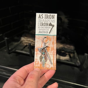 May include: A silver keychain with a small tomahawk charm and a quote that reads "As iron sharpens iron, so one person sharpens another."  Proverbs 27:17