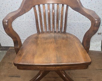 May include: A vintage wooden office chair with a curved back and armrests. The chair features a slatted backrest and a swivel base with small wheels. The wood has a warm, medium-brown tone, and the chair appears to be well-maintained.