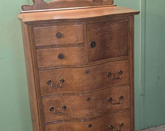 以下が含まれることがあります： 鏡付きのヴィンテージ木製ドレッサー。ドレッサーは明るい茶色の仕上げで、曲線的な引き出しと装飾的な金具が付いています。鏡は長方形で装飾的なフレームが付いています。ドレッサーの高さは約152cmです。