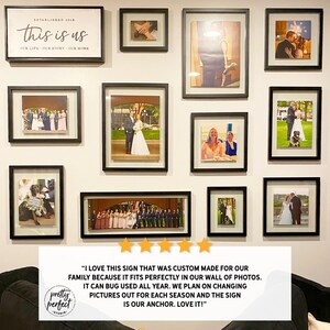 May include: A wall display of framed photographs and a sign that reads "this is us." The frames are black and contain various photos, including wedding and family portraits. The sign is white with black text.