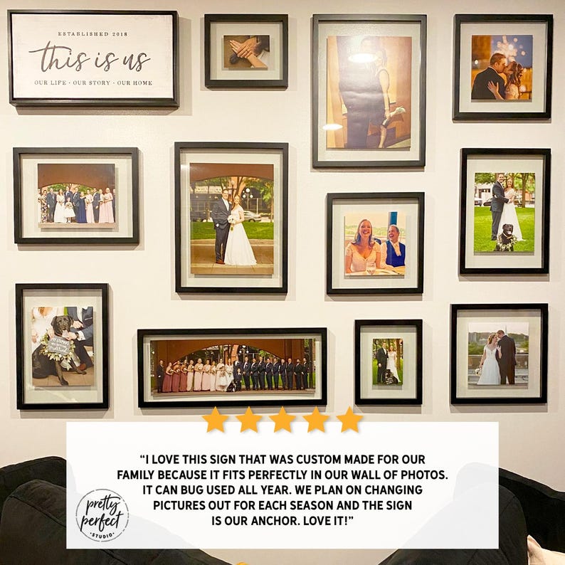 May include: A wall display of framed photographs and a sign that reads "this is us." The frames are black and contain various photos, including wedding and family portraits. The sign is white with black text.