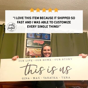 May include: A rectangular, off-white sign with the words "this is us" in a script font, with family names below. The sign also includes the phrases "Our Life, Our Home, Our Story" above the main text. The sign is held by a person.