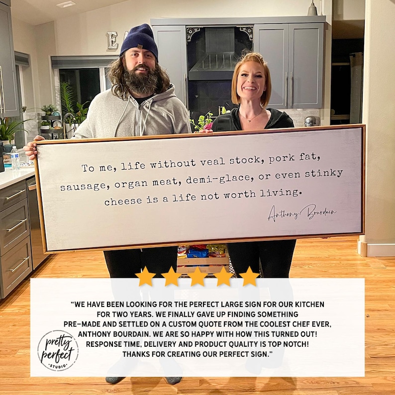 May include: A white wooden sign with a black frame and a quote from Anthony Bourdain that reads "To me, life without veal stock, pork fat, sausage, organ meat, demi-glace, or even stinky cheese is a life not worth living."
