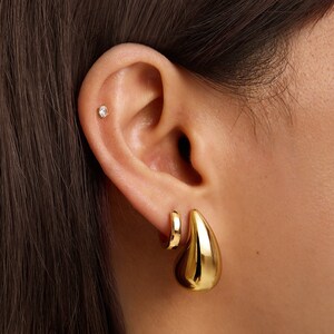 May include: A pair of gold earrings. One earring is a small hoop and the other is a larger teardrop shape.