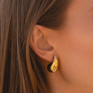 May include: A close-up of a person wearing a pair of gold hoop earrings. The earrings are large and have a smooth, rounded shape.