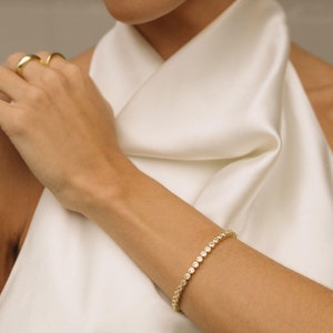 May include: A gold bracelet with small round clear stones. The bracelet is on a person's wrist.
