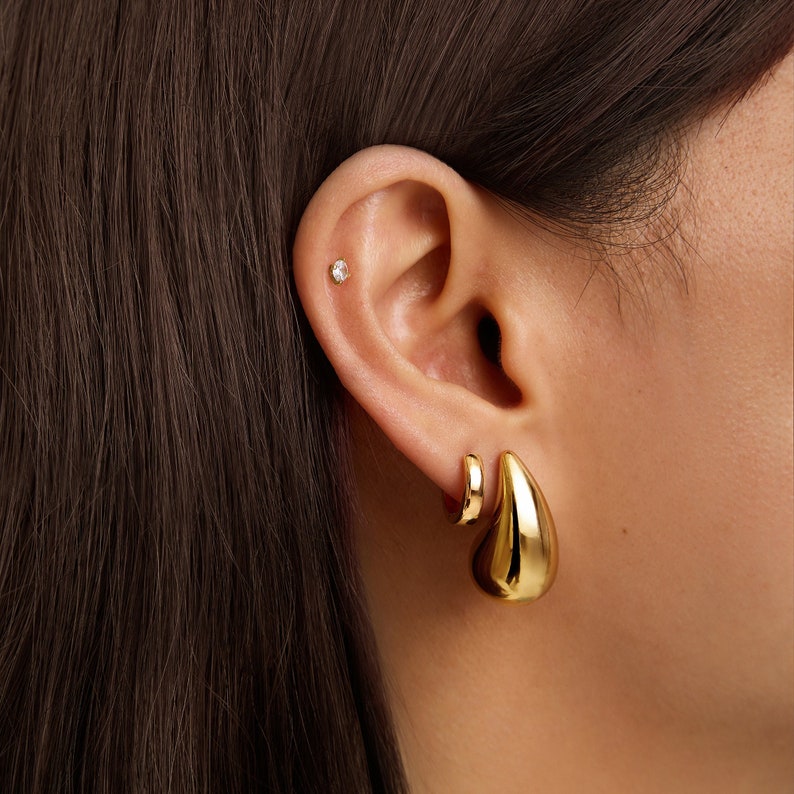 May include: A pair of gold earrings. One earring is a small hoop and the other is a larger teardrop shape.