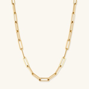 May include: A gold-toned chain necklace featuring elongated, rectangular paperclip-style links. The necklace has a polished, reflective surface and a uniform design throughout, with each link connected to the next in a continuous, repeating pattern.