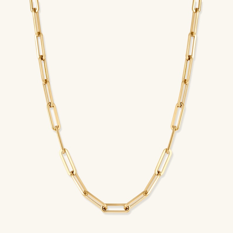 May include: A gold-toned chain necklace featuring elongated, rectangular paperclip-style links. The necklace has a polished, reflective surface and a uniform design throughout, with each link connected to the next in a continuous, repeating pattern.