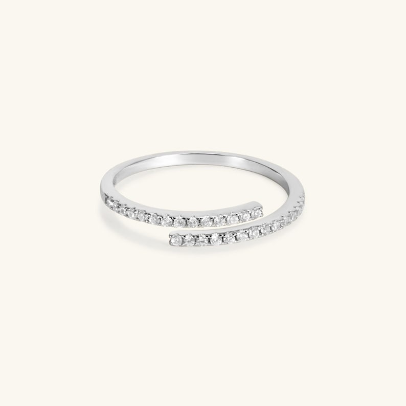 May include: A silver ring with a delicate design featuring two bands of small diamonds that intersect.