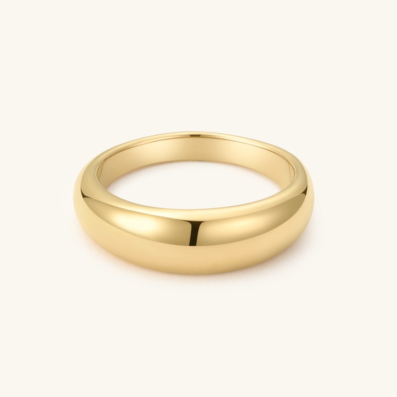 Op de afbeelding: Een gepolijste geelgouden ring met een glad, afgerond en koepelvormig oppervlak. De ring heeft een doorlopende, massieve metalen constructie met een hoogglanzende afwerking die het licht gelijkmatig weerkaatst over het ronde profiel.