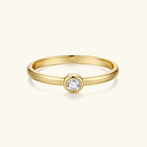 Puede incluir: Un anillo de banda de oro simple con un solo diamante redondo engastado en un engaste de bisel.