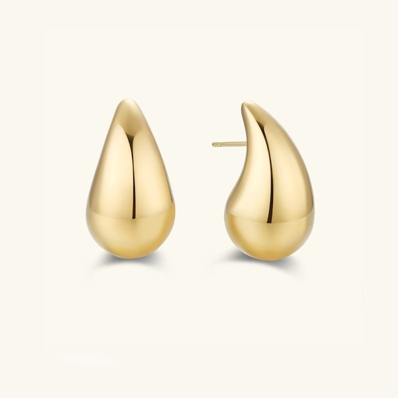 May include: A pair of gold teardrop-shaped earrings. The earrings are smooth and shiny.
