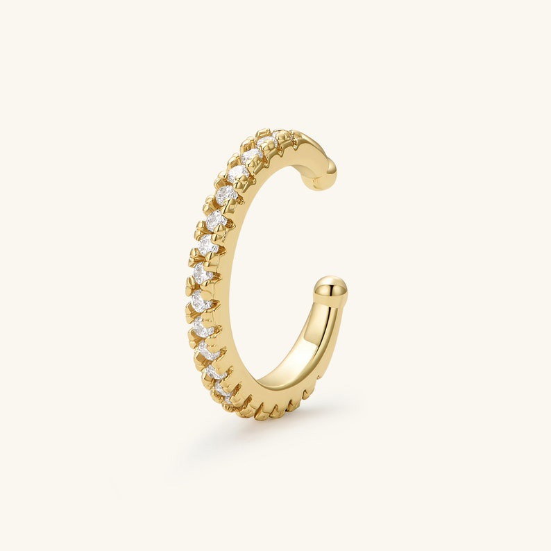 May include: A gold ear cuff with a row of clear cubic zirconia stones.