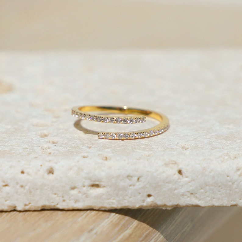 May include: A gold ring with a delicate, twisted design. The ring is set with small, clear stones that create a sparkling effect.