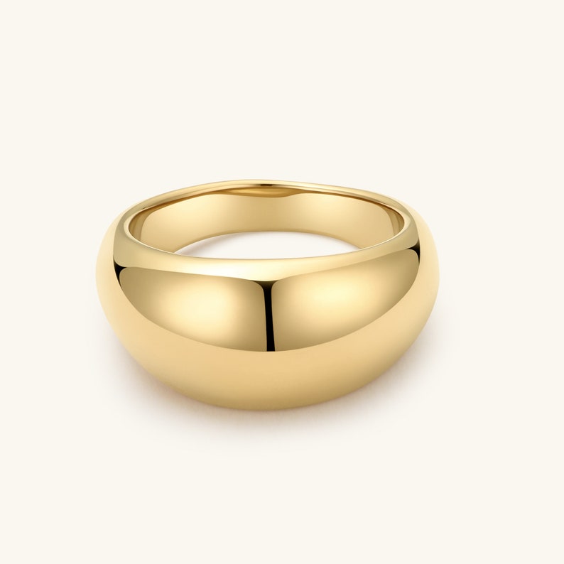 Op de afbeelding: Een gepolijste gouden dome-ring met een glad, afgerond oppervlak en een dikke, doorlopende band. Het metaal heeft een hoogglanzende, reflecterende afwerking die het licht opvangt, wat zorgt voor een strakke, solide en uniforme uitstraling over het hele sieraad.