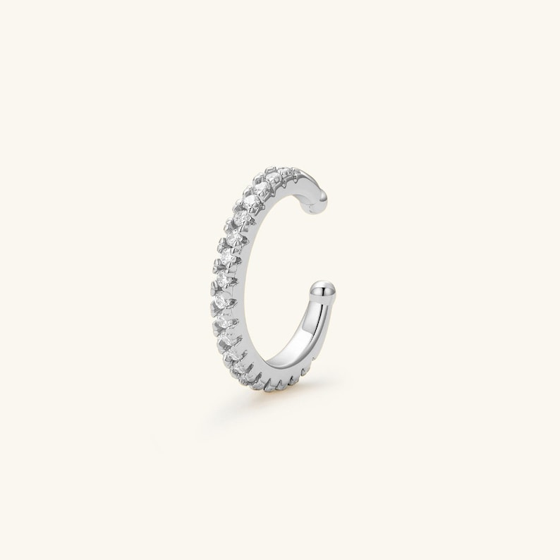 May include: A silver ear cuff with a row of clear cubic zirconia stones.