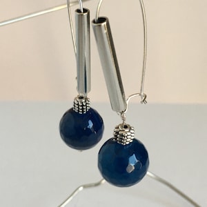 Könnte beinhalten: Ein Paar silberne Ohrhänger mit dunkelblauen Achat-Edelsteinkugeln. Die Ohrringe haben einen silbernen Schlauch und eine silberne Perle mit einem strukturierten Design.