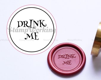 May include: A white round sticker with black text that reads "DRINK ME" with a pink outline. A red wax seal with the same text is next to the sticker.