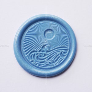 May include: A blue wax seal with a sun and waves design. The seal is round and has a raised design.