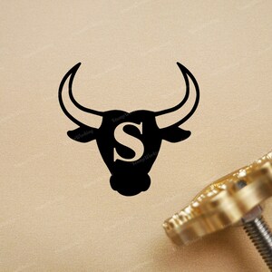 May include: A black silhouette of a bull with the letter "S" in the center, on a gold background. A gold metal stamp with a bull design is also shown.