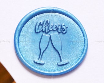 May include: A blue wax seal with the word "Cheers" and a silhouette of two champagne glasses.