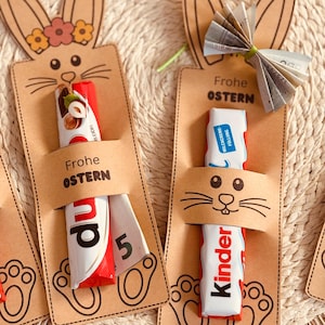 Könnte beinhalten: Oster-Geschenkanhänger mit Hasenmotiven. Jeder Anhänger enthält einen Kinder-Schokoriegel, mit dem Aufdruck "Frohe Ostern". Die Anhänger sind aus braunem Karton gefertigt und haben Pfotenabdrücke am unteren Rand.