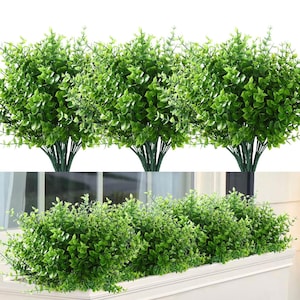 May include: Three artificial green bush plants with small leaves. The plants are shown in a white window box.