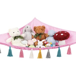 May include: A pink fabric hammock with tassels hanging from the edges. The hammock is filled with stuffed animals, including a bear, a bunny, a hippo, and a mushroom.