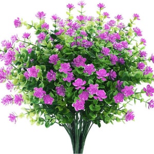 以下が含まれることがあります： 小さなピンクの花と緑の葉を持つ人工の花のブーケ。花は房状に配置されており、豊かで豪華な外観を作り出しています。