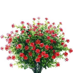 May include: A bouquet of artificial red flowers with green leaves. The flowers are small and clustered together, creating a full and lush look.