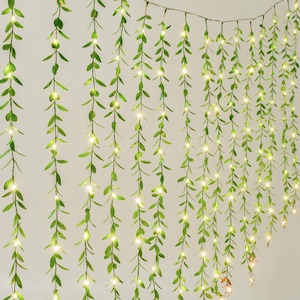 May include: A string of fairy lights with green leaves, creating a curtain of lights. The lights are warm white and the leaves are a vibrant green.