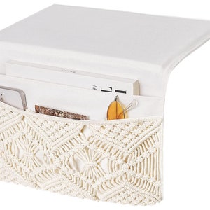 May include: A white crocheted storage organiser with a flap top. The organiser has a pocket on the front and is filled with items such as a book, a phone, and sunglasses.