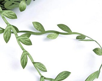 Puede incluir: Una guirnalda de hojas verdes enrollada. La guirnalda presenta pequeñas hojas detalladas unidas a un tallo flexible. Las hojas son de un color verde apagado, y la guirnalda probablemente está hecha de tela o papel.