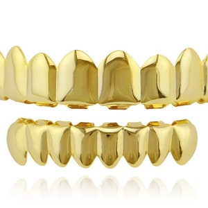 May include: A set of gold-colored teeth grillz, featuring a top and bottom row. The grillz have a shiny, reflective surface and are designed to fit over the natural teeth. The overall aesthetic is bold and eye-catching.