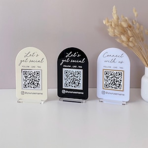 Op de afbeelding: Drie sociale media borden van acryl in crème, zwart en wit. Elk bord heeft een QR-code, de tekst "Let's get social" of "Connect with us" en de Instagram-gebruikersnaam "@yourusername".